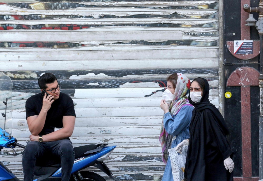 An Iranian youth talks on the phone as he watches women wearing protective masks walk by on a street of the capital Tehran, on May 09, 2020, amid the novel coronavirus pandemic. / AFP / ATTA KENARE