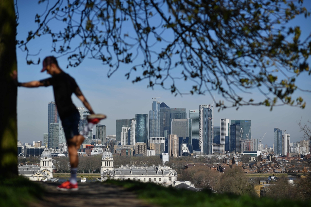 (FILES) In this file photo taken on March 23, 2020 London's financial district Canary Wharf is seen as a man exercises in Greenwich Park in South London on March 23, 2020, as people come to terms with the governments request for social distancing as the C