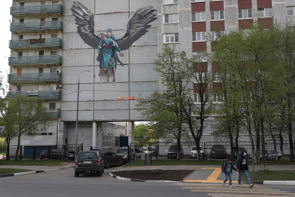 People wearing protective face masks cross a street near an apartment block, which is decorated with a mural dedicated to medical specialists involved in the fight against the coronavirus disease (COVID-19), in Odintsovo outside Moscow, Russia May 14, 202