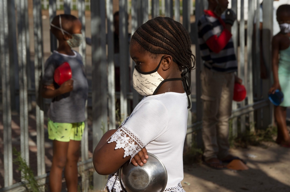 Children wait in lines at a crèche in Langa, near Cape Town on May 14, 2020, to receive a meal, which will include soup made by Woodstock Breweries, which is part of a project to feed people made vulnerable under the lockdown in South Africa, as a result 