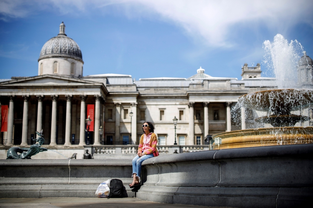 A woman enjoys the sunshine by water fountains in Trafalgar Square in central London on May 18, 2020. AFP / Tolga Akmen 