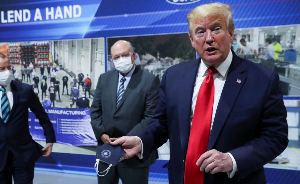 U.S. President Donald Trump holds a protective face mask with a presidential seal on it that he said he had been wearing earlier in his tour as Ford Motor Company CEO Jim Hackett looks on at the Ford Rawsonville Components Plant that is manufacturing vent