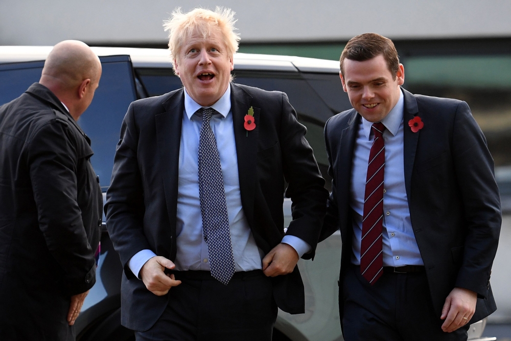 (FILES) In this file photo taken on November 07, 2019 Britain's Prime Minister Boris Johnson (C) is greeted by Conservative party candidate for Moray, Douglas Ross (R) as he arrives for a general election campaign visit to Diageo's Roseisle Distillery nea