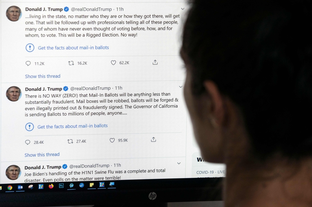 TOPSHOT - This illustration photo shows an editor in Los Angeles looking at the official Twitter account of US President Donald Trump on May 26, 2020, with two tweets by the president under which Twitter posted a link reading 