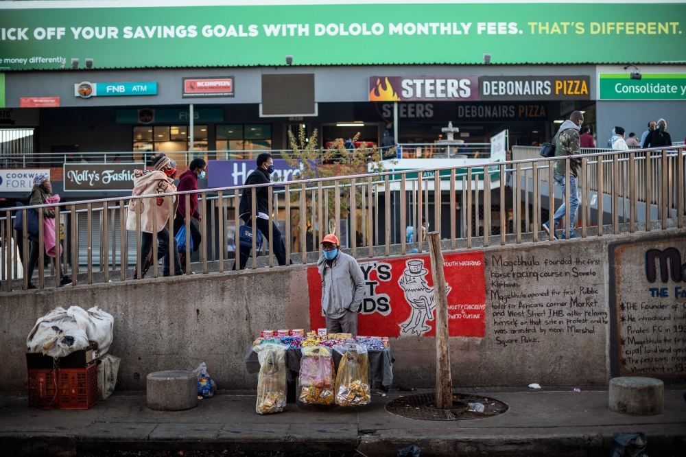 An informal vendor sets up his stall while commuters wearing face masks as a preventive measure against the spread of the COVID-19 coronavirus arrive at the Bara taxi rank in Soweto, Johannesburg, on June 1, 2020. / AFP / Michele Spatari
