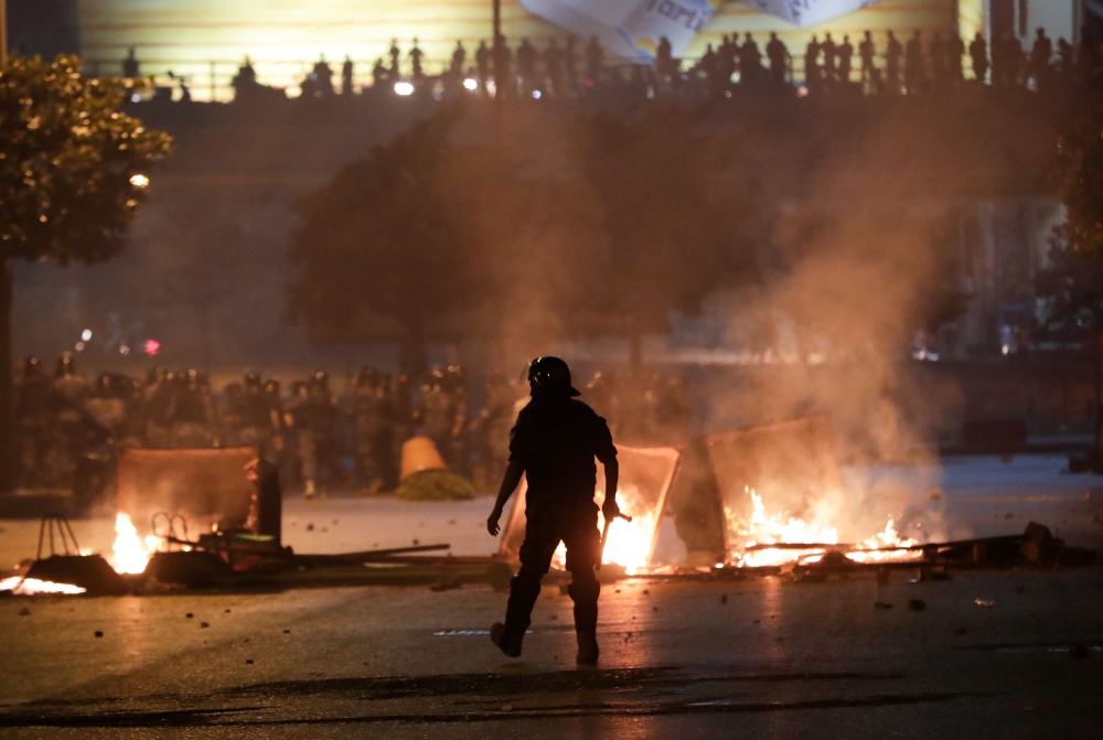 A member of the Lebanese security forces walks toward rubbish containers set ablaze by anti-government protesters, during a demonstration against dire economic conditions, under the Fuad Shehab bridge known as the Ring, in the capital Beirut, late on June