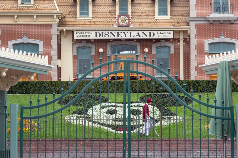 (FILES) In this file photo taken on March 14, 2020 an employee cleans the grounds behind the closed gates of Disneyland Park on the first day of the closure of Disneyland and Disney California Adventure theme parks as fear of the spread of coronavirus con