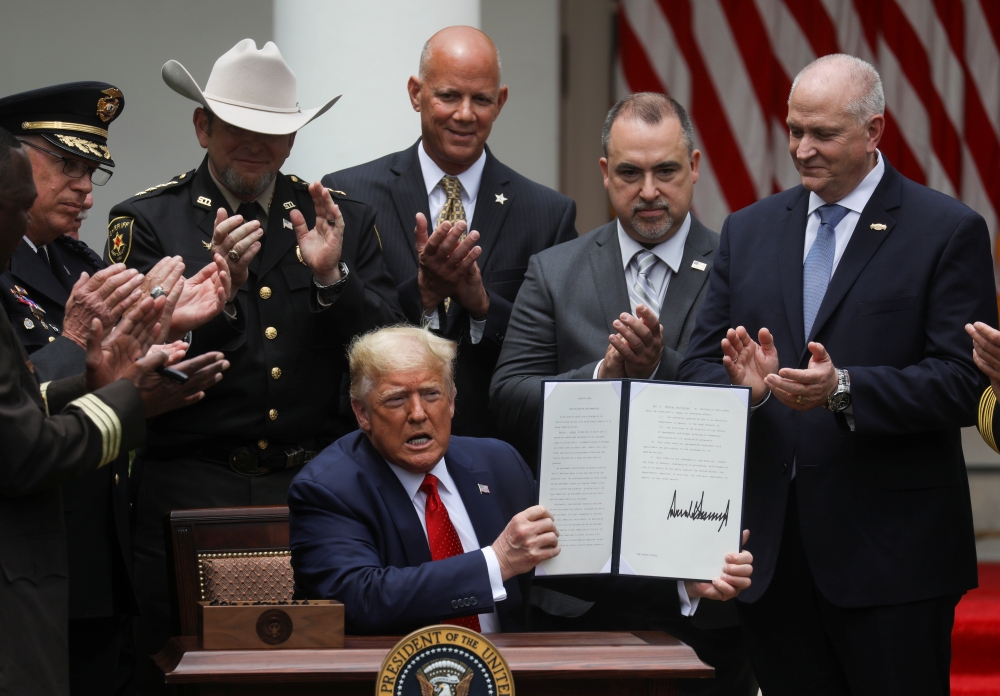U.S. President Donald Trump is applauded by law enforcement leaders surrounding him as he holds up an executive order on police reform after signing it during an event in the Rose Garden at the White House in Washington, U.S., June 16, 2020. REUTERS/Leah 