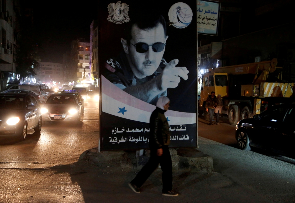 FILE PHOTO: A woman walks past a poster depicting Syria's President Bashar al-Assad in Damascus, Syria, March 5, 2020. REUTERS/Yamam Al Shaar/File Photo