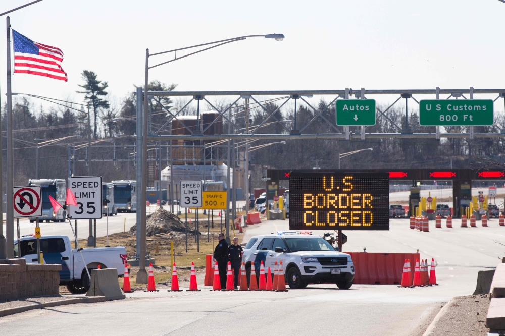 :(FILES) In this file photo taken on March 22, 2020 US Customs officers stand beside a sign saying that the US border is closed at the US/Canada border in Lansdowne, Ontario. Ottawa and Washington are in talks to extend the closure of the Canada-US border