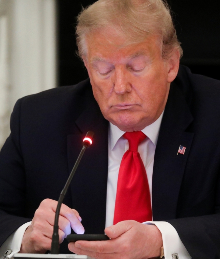 U.S. President Donald Trump taps the screen on a mobile phone at the approximate time a tweet was released from his Twitter account, during a roundtable discussion on the reopening of small businesses in the State Dining Room at the White House in Washing