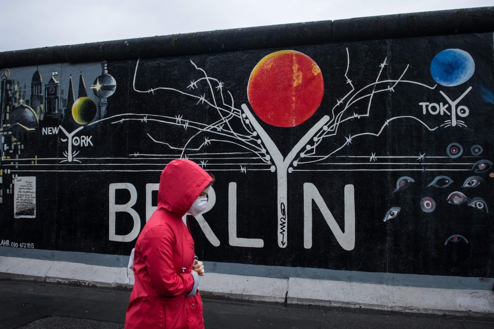 A woman with a protective face mask passes a mural on parts of former Berlin Wall at East Side Gallery in Berlin, on June 20, 2020. / AFP / STEFFI LOOS
