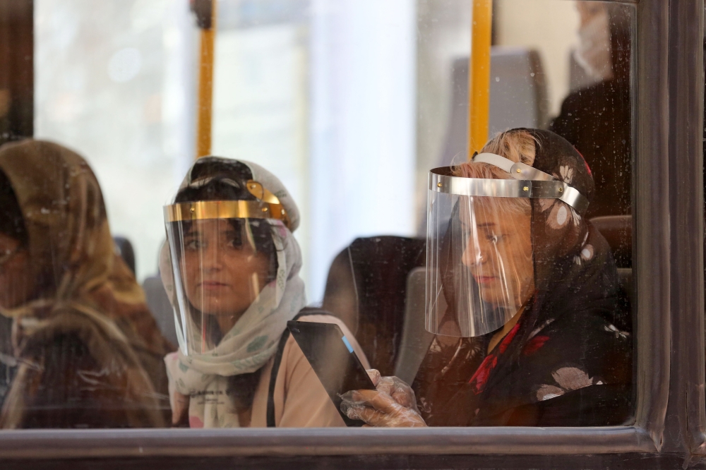 Passengers, wearing face shields due to the COVID-19 coronavirus, sit inside a bus in the Iranian capital Tehran on June 22, 2020. / AFP / ATTA KENARE