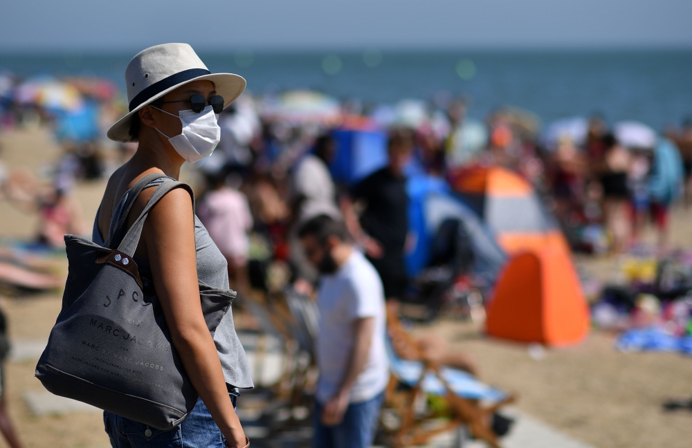 A woman wearing a face mask or covering as a precautionary measure against spreading COVID-19, arrives on the beach in the sea in Southend on Sea, south east England, on June 24, 2020. AFP / Ben STANSALL
