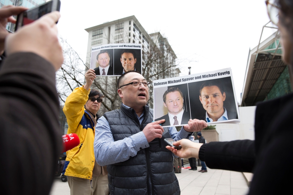 (FILES) In this file photo taken on March 06, 2019 Louis Huang of Vancouver Freedom and Democracy for China holds photos of Canadians Michael Spavor and Michael Kovrig, who are being detained by China, outside British Columbia Supreme Court, in Vancouver,