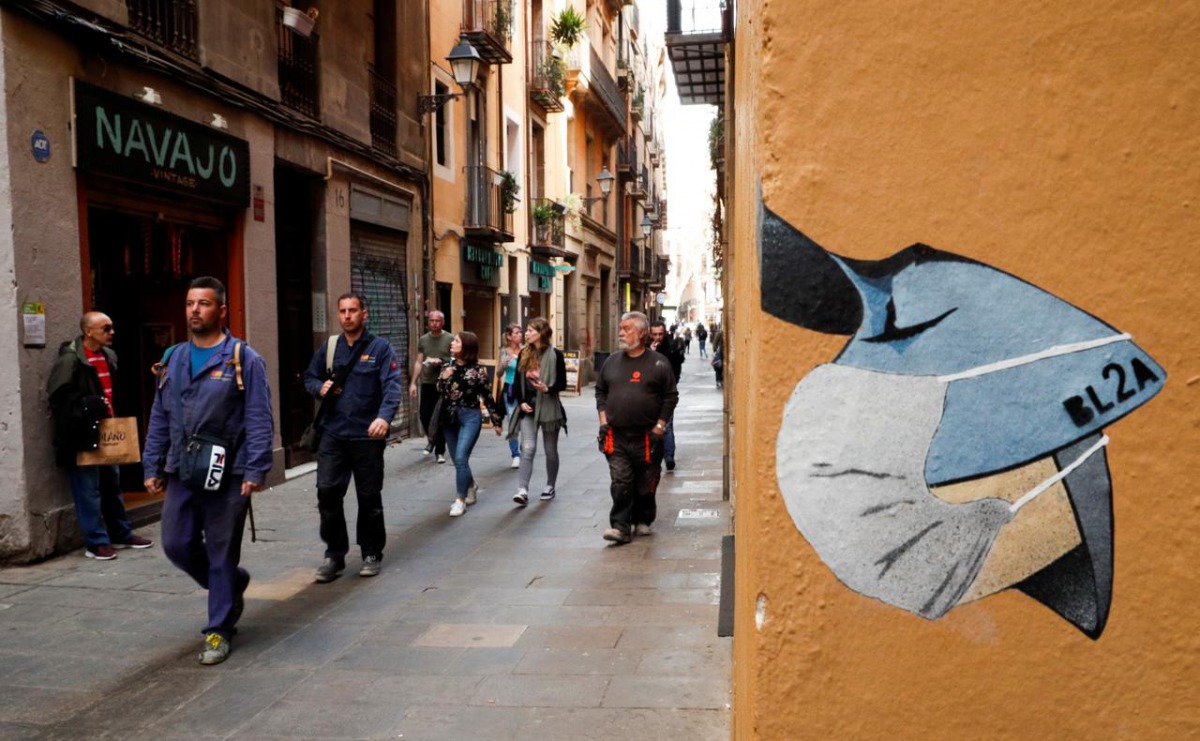 People pass near a drawing of a person wearing a mask in a wall, due to the coronavirus outbreak, in central Barcelona, Spain, March 12, 2020. REUTERS/Albert Gea