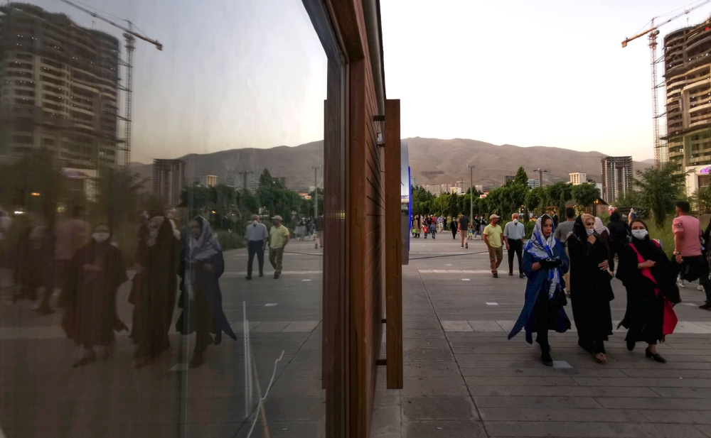 Iranians wearing protective masks walk along a street near the artificial Chitgar lake in the capital Tehran, amid the novel coronavirus pandemic crisis on July 3, 2020. / AFP / ATTA KENARE