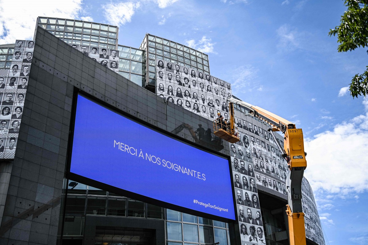 Workers paste portraits of healthcare workers on the facade of the Opera Bastille, at the initiative of the collective #ProtegeTonSoignant to pay tribute to caregivers in first ligne during the Covid-19 epidemic, next to a screen reading 
