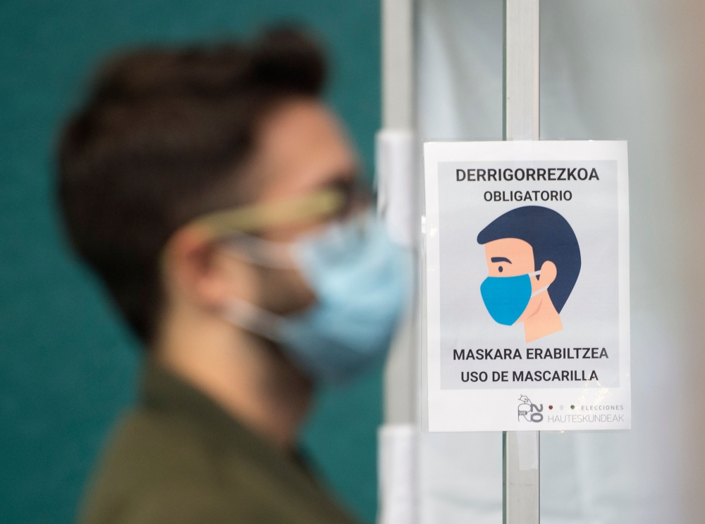 A man wearing a face mask stands next to a sign reading 