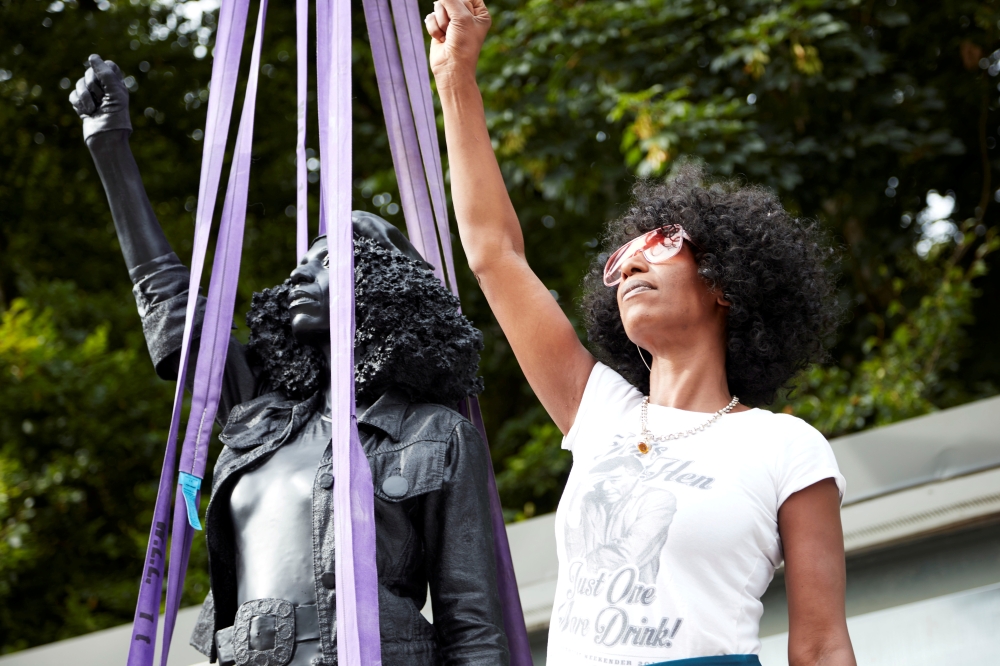 Jen Reid poses next to a sculpture by Marc Quinn portraying her, titled 'A Surge of Power (Jen Reid) 2020', in London, Britain July 14, 2020, in this image obtained from social media. Picture taken July 14, 2020. Courtesy of Marc Quinn Studio/via REUTERS