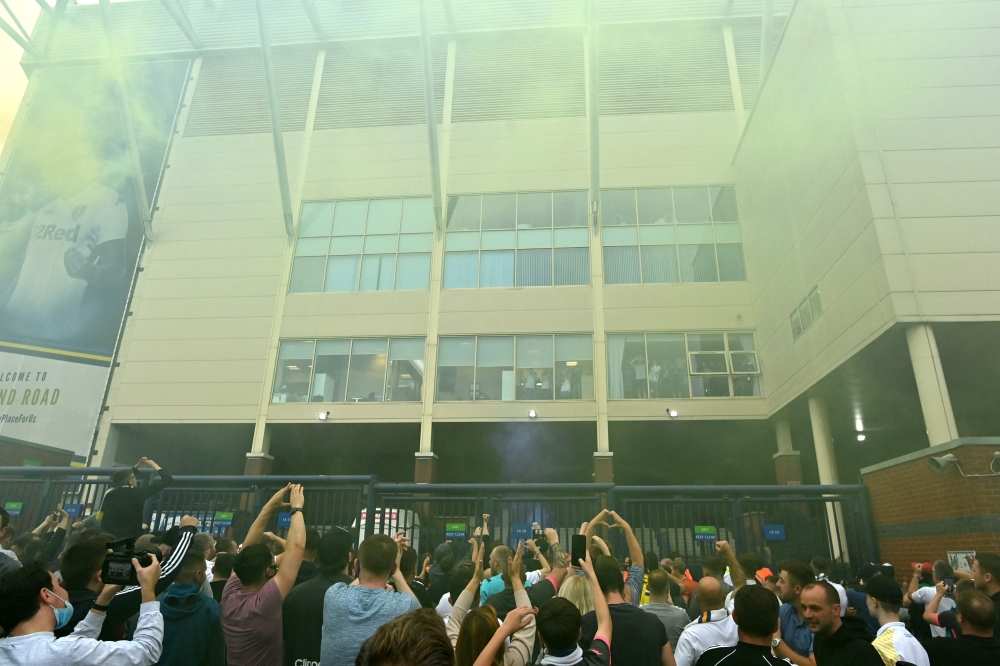 Leeds United players at a window inside the stadium gesture to supporters gathering outside their Elland Road ground to celebrate the club's return to the Premier League after a gap of 16 years, in Leeds, northern England on July 17, 2020. Leeds United we