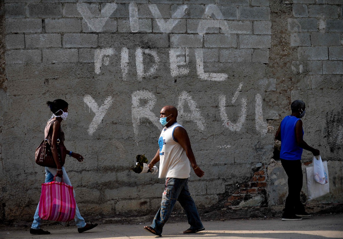Afro-Cubans wear face masks as a preventive measure against the spread of the novel coronavirus, COVID-19, as they walk past a graffiti reading 