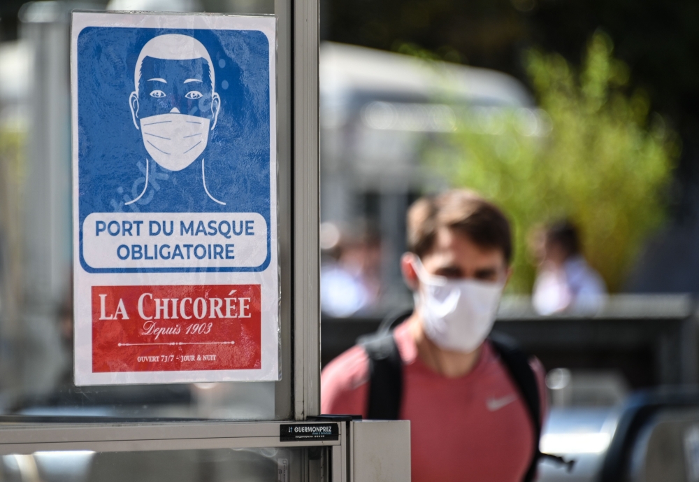 A man wearing a protective face mask due to the COVID-19 coronavirus pandemic, walks next to a mandatory wearing mask sign in front of a shop in a pedestrian street in Lille on July 20, 2020, as masks become mandatory in all indoor public spaces. AFP / DE