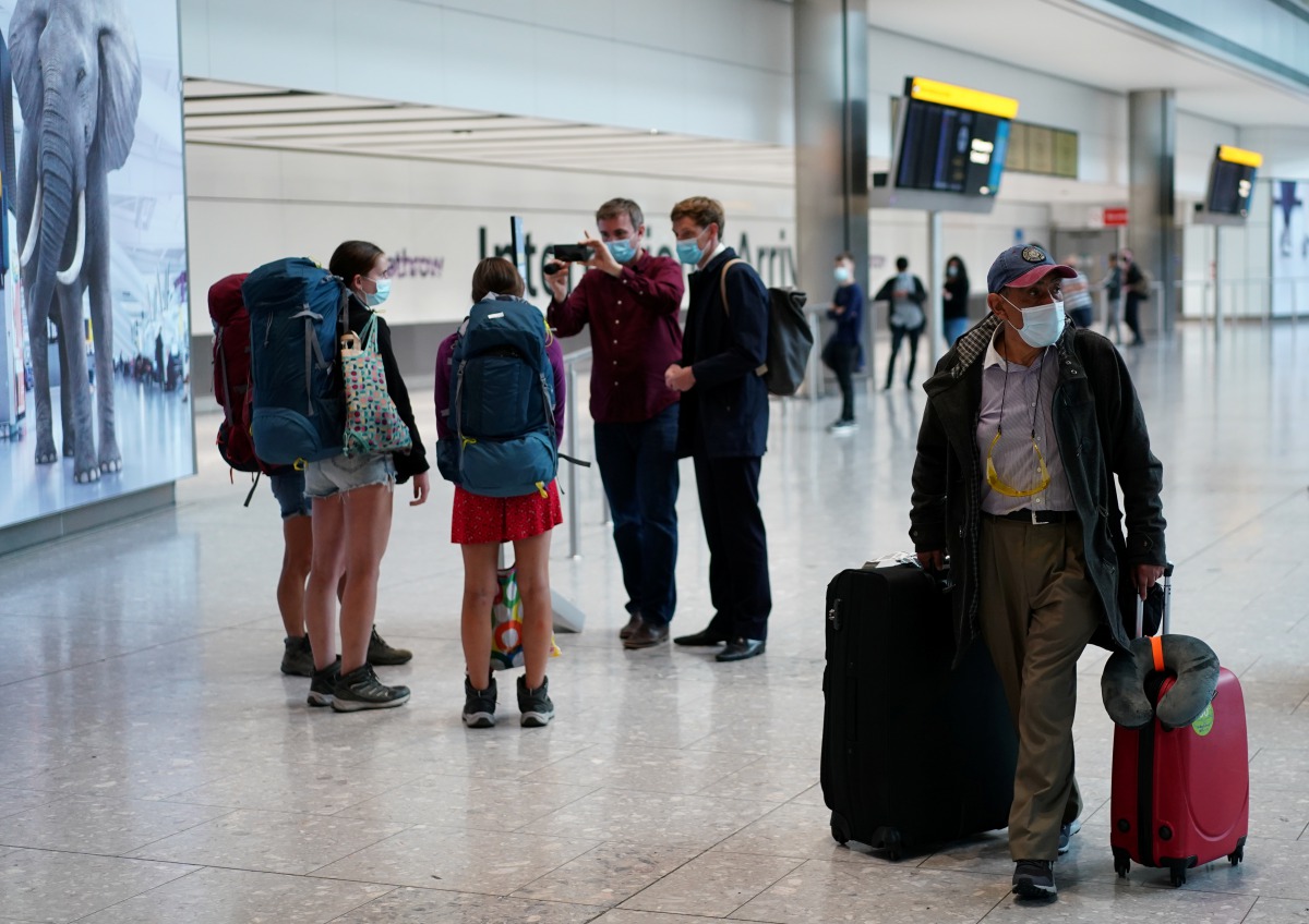 A man carries a luggage as reporters wearing face masks speak to travellers arriving from MADRID at the Terminal 5 at Heathrow Airport, as the spread of the?coronavirus?disease (COVID-19) continues, in London, Britain, July 26, 2020. REUTERS/Henry Nicholl