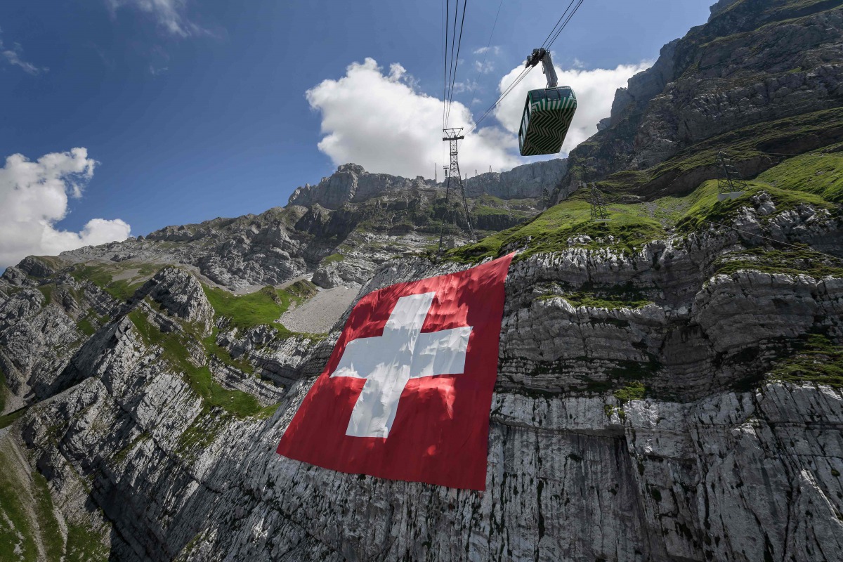 A picture taken on on July 31, 2020 near Schwagalp, eastern Switzerland, shows a huge 6,400 square meters Swiss flag hanging on the rock face of mountain Saentis on the eve of Swiss national day. / AFP / Fabrice COFFRINI
