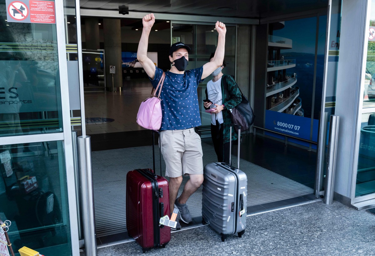 A traveller, mask-clad due to the COVID-19 coronavirus pandemic, arriving on one of the first flights from Britain gestures as he walks with luggage out of the terminal at Cyprus' Larnaca International Airport on August 1, 2020. / AFP / Iakovos Hatzistavr