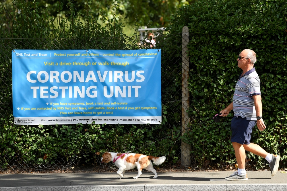 A man walks his dog past a poster promoting the coronavirus disease (COVID-19) testing at local mobile test centres, in Hounslow, London, Britain August 4, 2020. REUTERS/Toby Melville