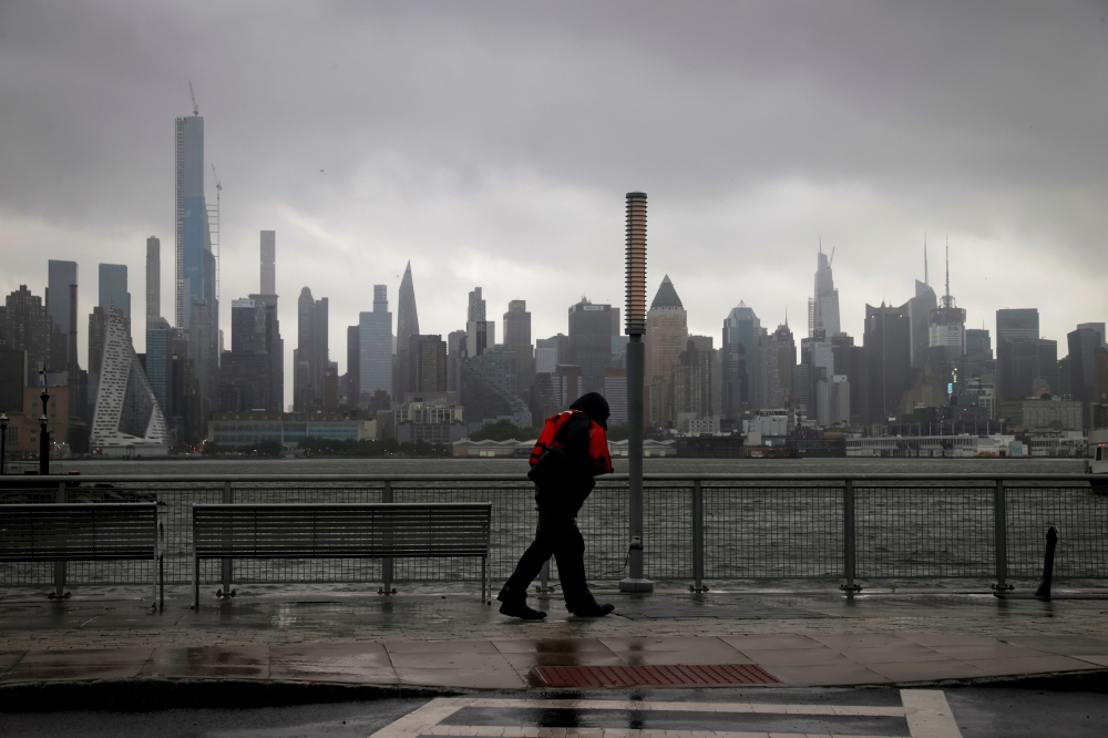A man walks into heavy wind and rain along the waterfront of the Hudson River in front of the New York City skyline during Tropical Storm Isaias in Weehawken, New Jersey, U.S., August 4, 2020. REUTERS/Mike Segar