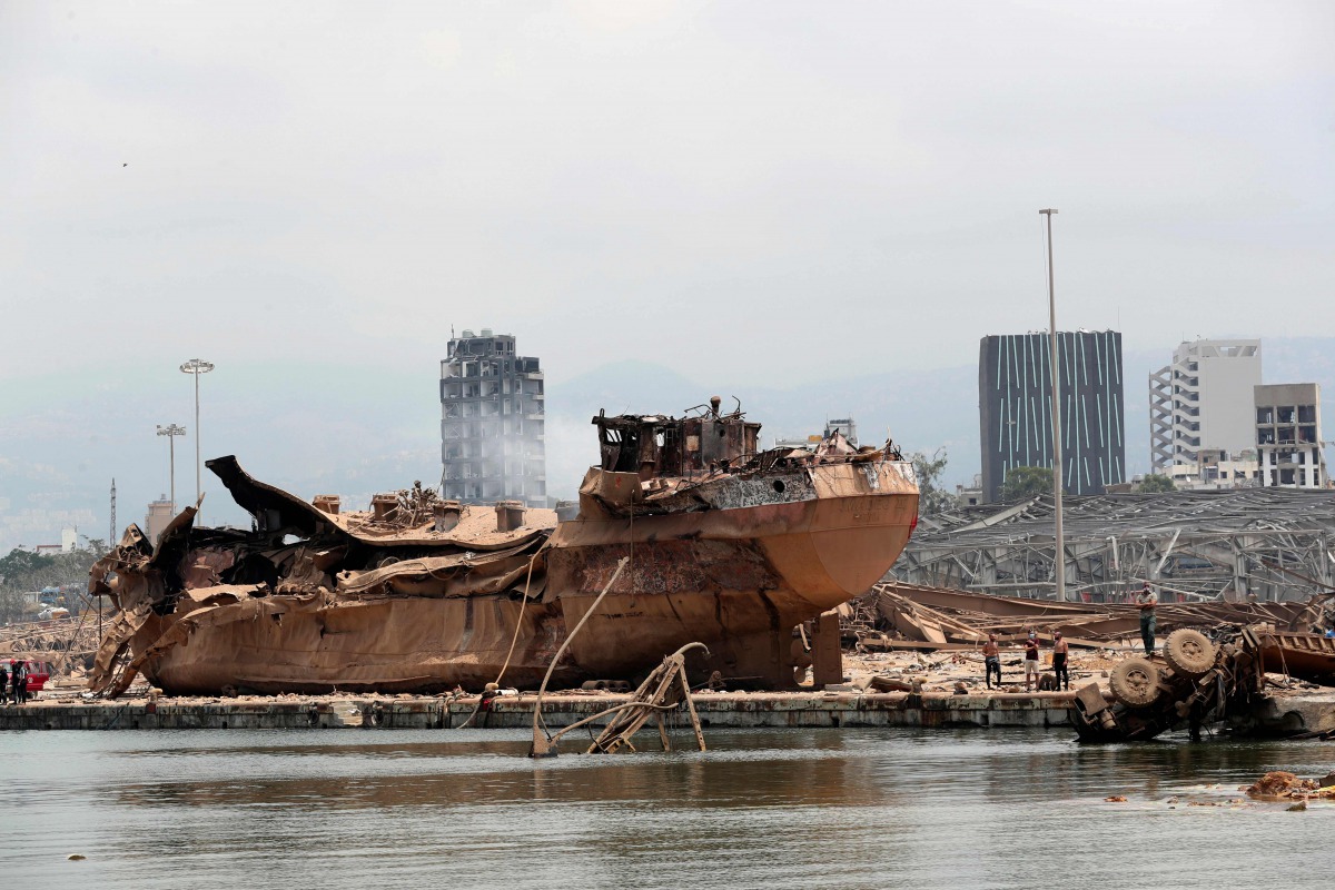People stand by the wreckage of a ship at the devastated site of the explosion in the port of Beirut on August 6, 2020 two days after a massive explosion devastated the Lebanese capital in a disaster that has sparked grief and fury. / AFP / POOL / Thibaul
