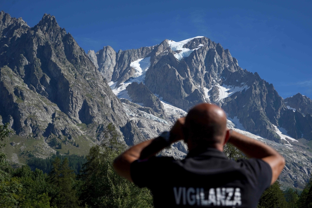 A security officer looks through binoculars at the Planpincieux glacier in Courmayeur village, Val Ferret, northwestern Italy on August 8, 2020. Several dozen people have been evacuated in northwestern Italy as a huge chunk of a glacier in the Mont Blanc 