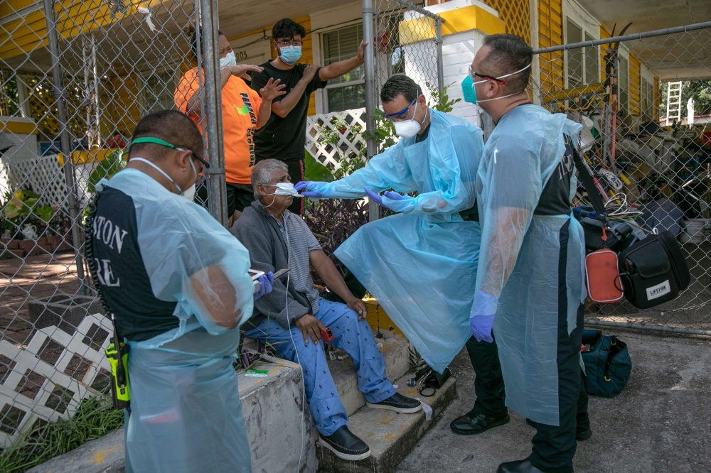 An EMS medic checks the temperature of a possible Covid-9 patient before transporting him to the hospital on August 13, 2020 in Houston, Texas. Several of the man's family members had also tested positive. The Latino community in Houston has been especial