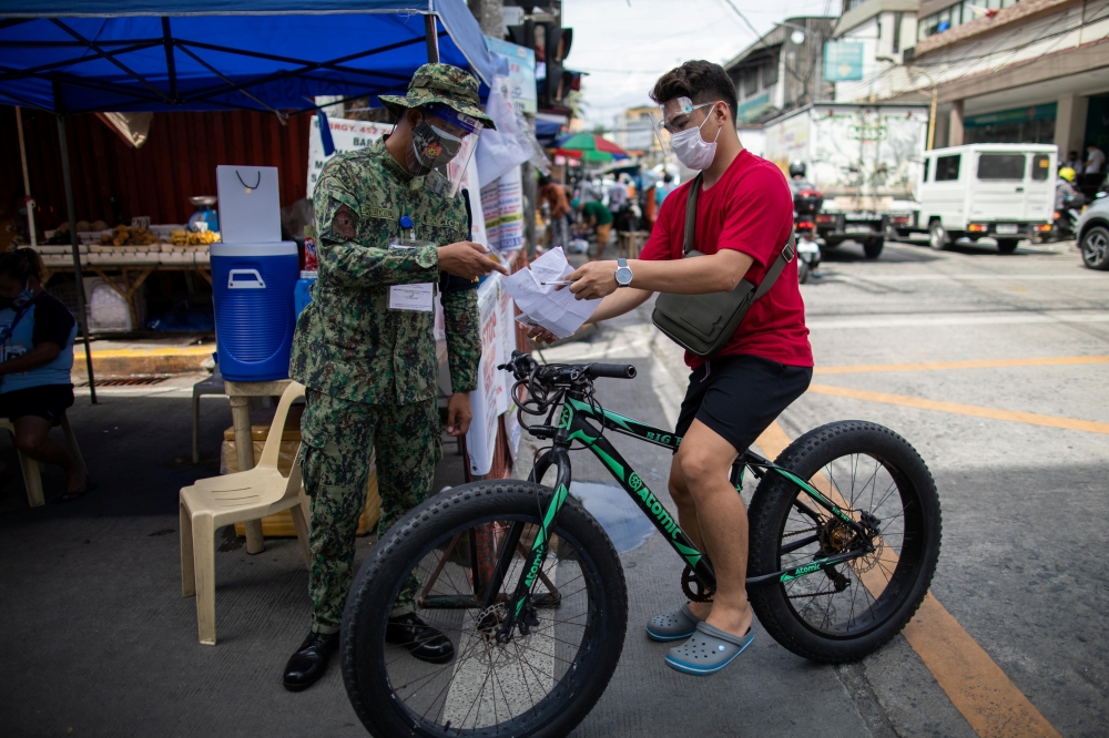 A police officer checks a bicycle rider's quarantine pass at a checkpoint placed amid the reimposed strict lockdown to curb coronavirus disease (COVID-19) infections, in Manila, Philippines, August 17, 2020. REUTERS/Eloisa Lopez