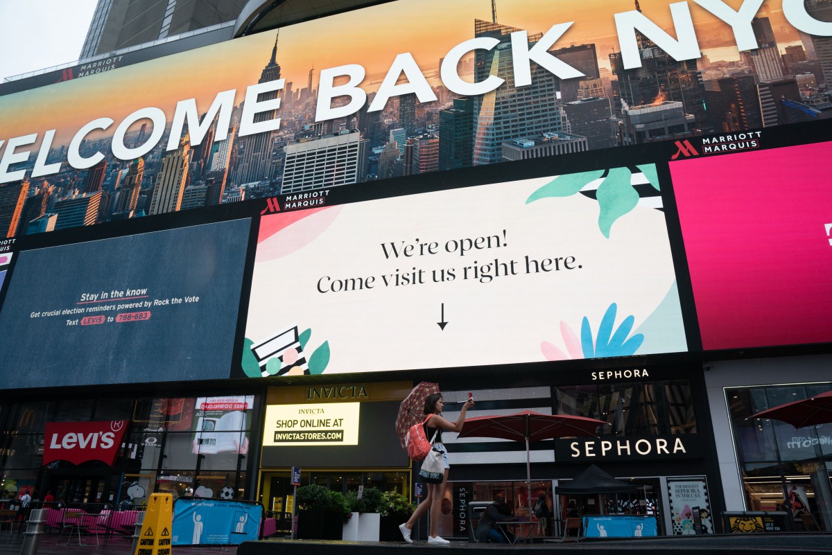 A tourist takes a selfie video underneath a billboard welcoming people back to NYC in Times Square on August 16, 2020 in New York. / AFP / Bryan R. Smith