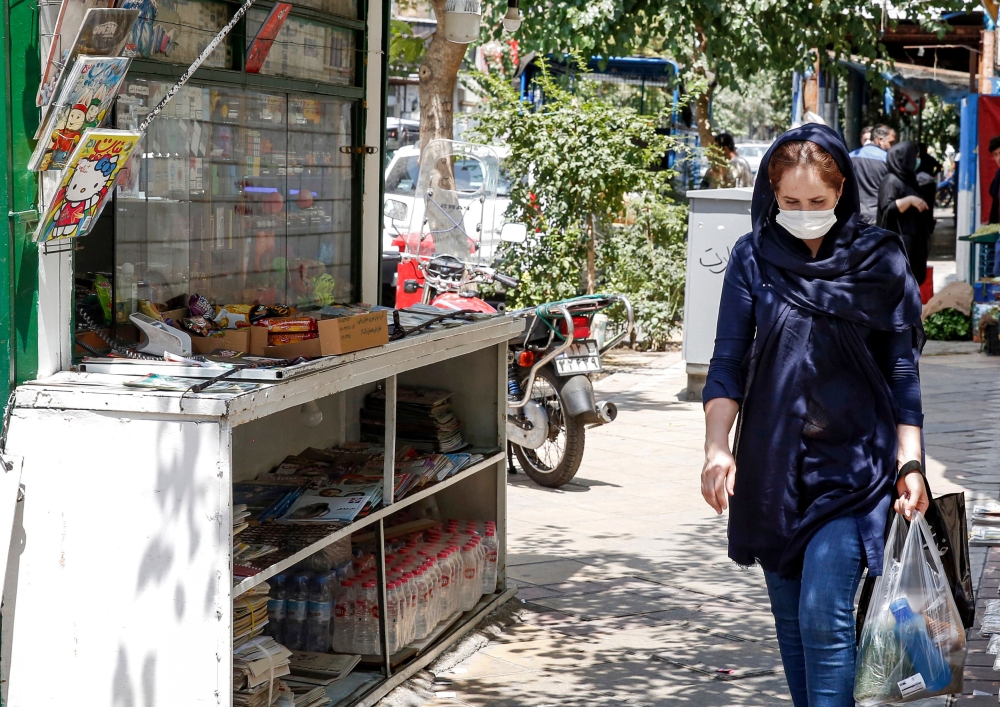 A woman clad in mask due to COVID-19 coronavirus pandemic walks past a newspaper stall in Iran's capital Tehran on August 15, 2020.  AFP 
