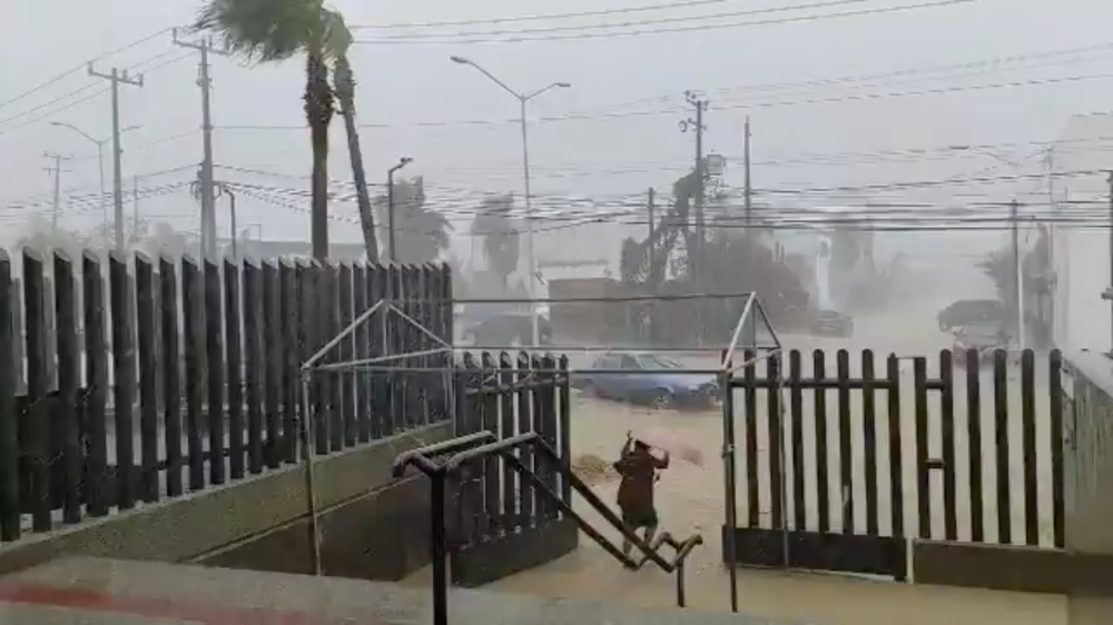 A woman walks under her umbrella while a car moves along a flooded road during Hurricane Genevieve in Los Cabos, Baja California Del Sur, Mexico August 19, 2020, in this still image obtained from video provided on social media. 