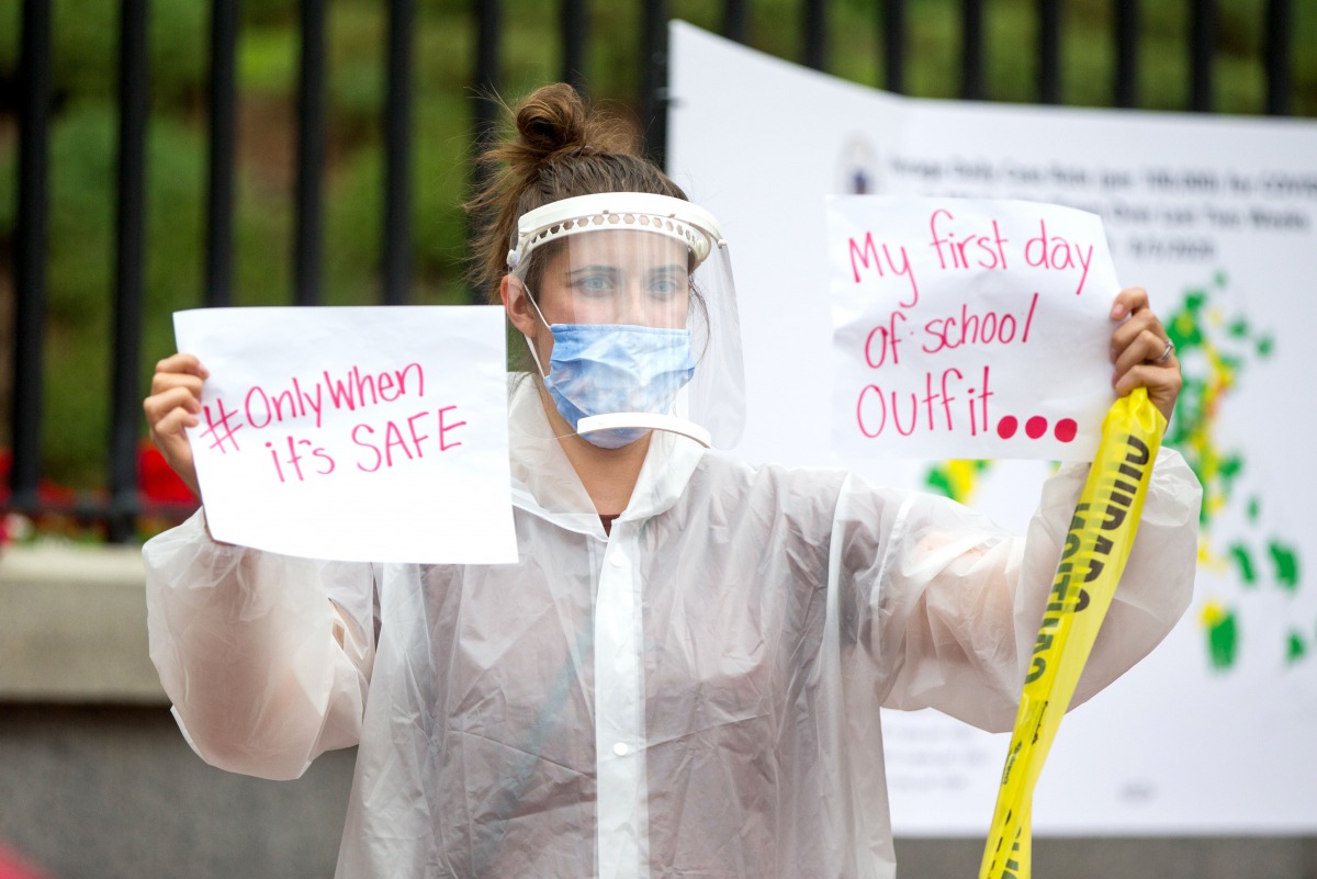 BOSTON, MA - AUGUST 19: A woman in personal protective equipment (PPE) holds up signs at a standout protest organized by the American Federation of Teachers at the Massachusetts State House on August 19, 2020, in Boston, Massachusetts. Scott Eisen/Getty I
