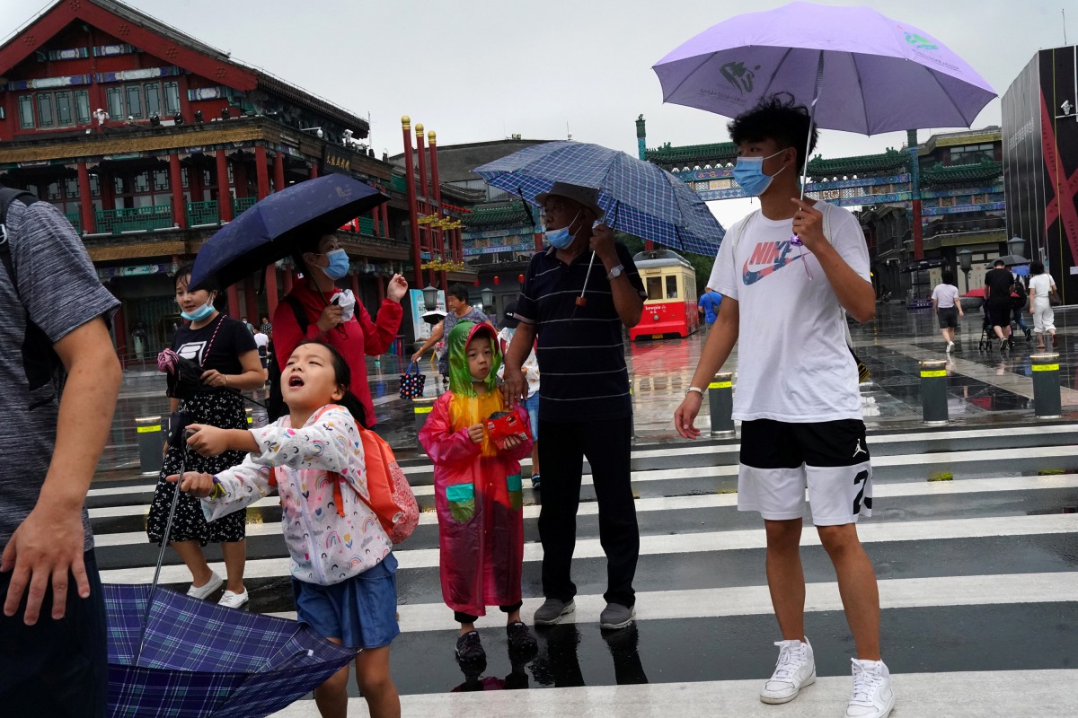 People wearing face masks walk near Qianmen Street on a rainy day, following the coronavirus disease (COVID-19) outbreak, in Beijing, China August 18, 2020. REUTERS/Tingshu Wang

