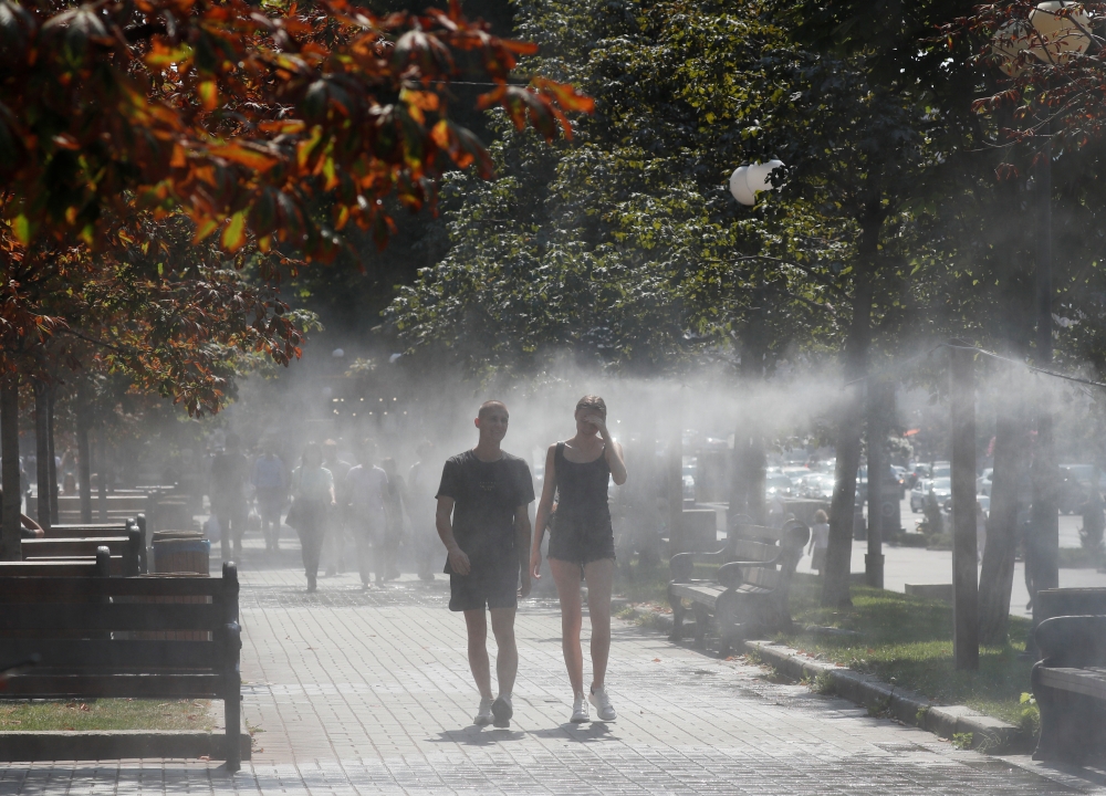 People walk through a water sprinkler on a hot summer day in central Kyiv, Ukraine August 21, 2020. REUTERS/Gleb Garanich