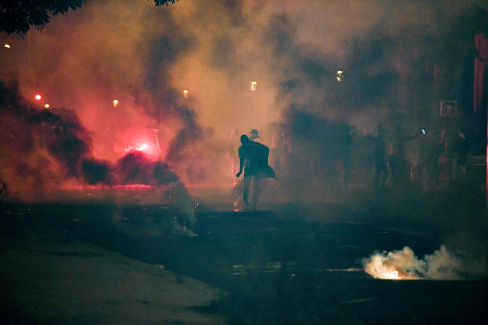 A man stands in tear gas smokes fired by French anti-riot policemen escorting Paris Saint-Germain (PSG) supporters around the Parc des Princes stadium on August 23, 2020. AFP / Alain JOCARD