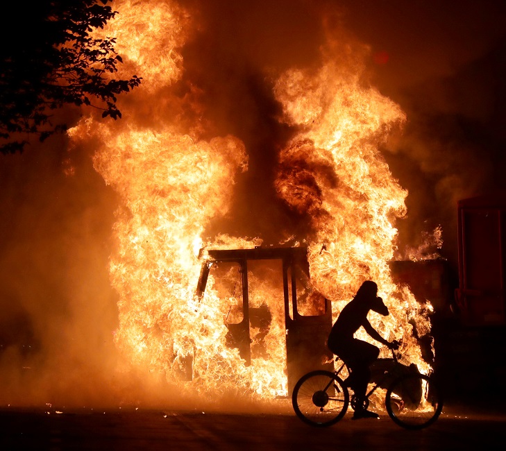 A man on a bike rides past a city truck on fire outside the Kenosha County Courthouse in Kenosha, Wisconsin, U.S., during protests following the police shooting of Black man Jacob Blake August 23, 2020. The picture was taken on August 23, 2020. Mike De Si
