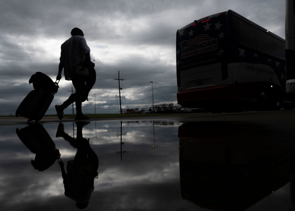 A woman rolls a suitcase as she walks to board a bus for evacuation before the arrival of hurricane Laura in Lake Charles, Louisiana on August 25, 2020 amid the coronavirus pandemic. / AFP / Andrew CABALLERO-REYNOLDS