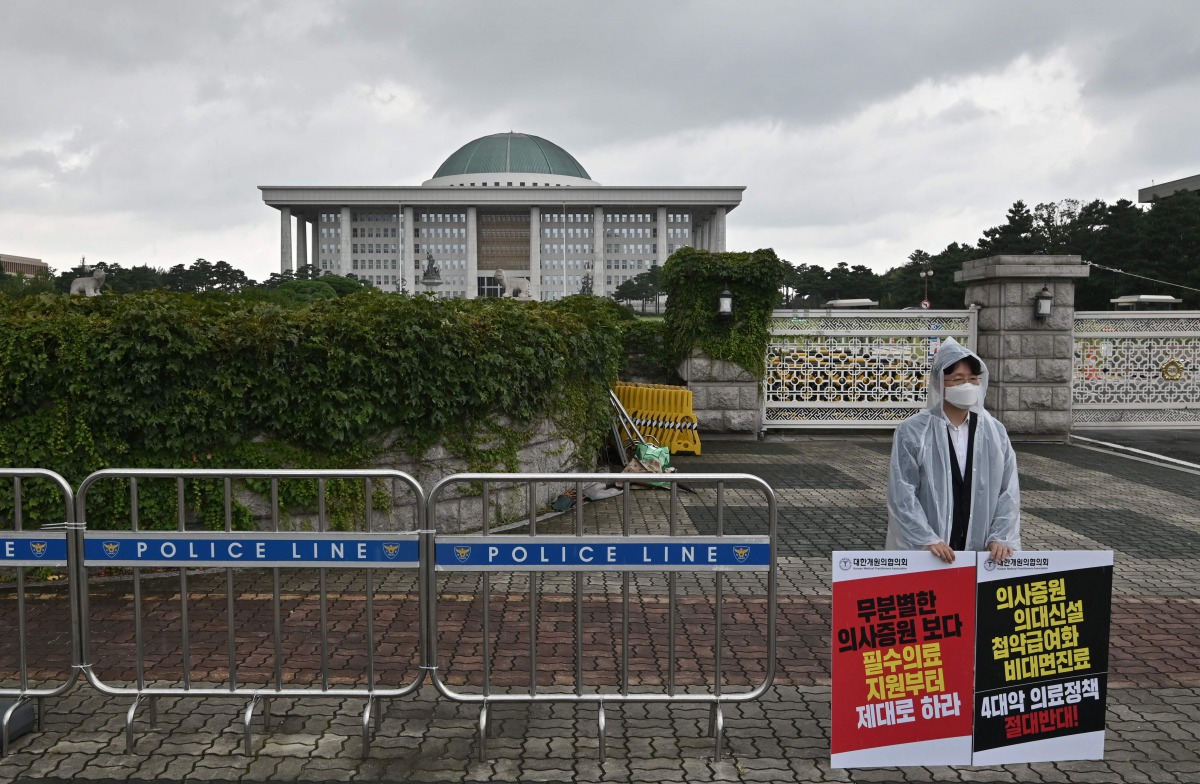 A South Korean medical doctor holds placards to protest against a government proposal to increase its annual intake of medical students, in front of the National Assembly in Seoul on August 27, 2020.  / AFP / Jung Yeon-je
