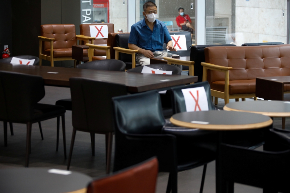 A man wearing a protective face mask sits as signs are attached to chairs to keep social distancing at a cafe, amid the coronavirus disease (COVID-19) pandemic in Seoul, South Korea, August 27, 2020. REUTERS/Kim Hong-Ji