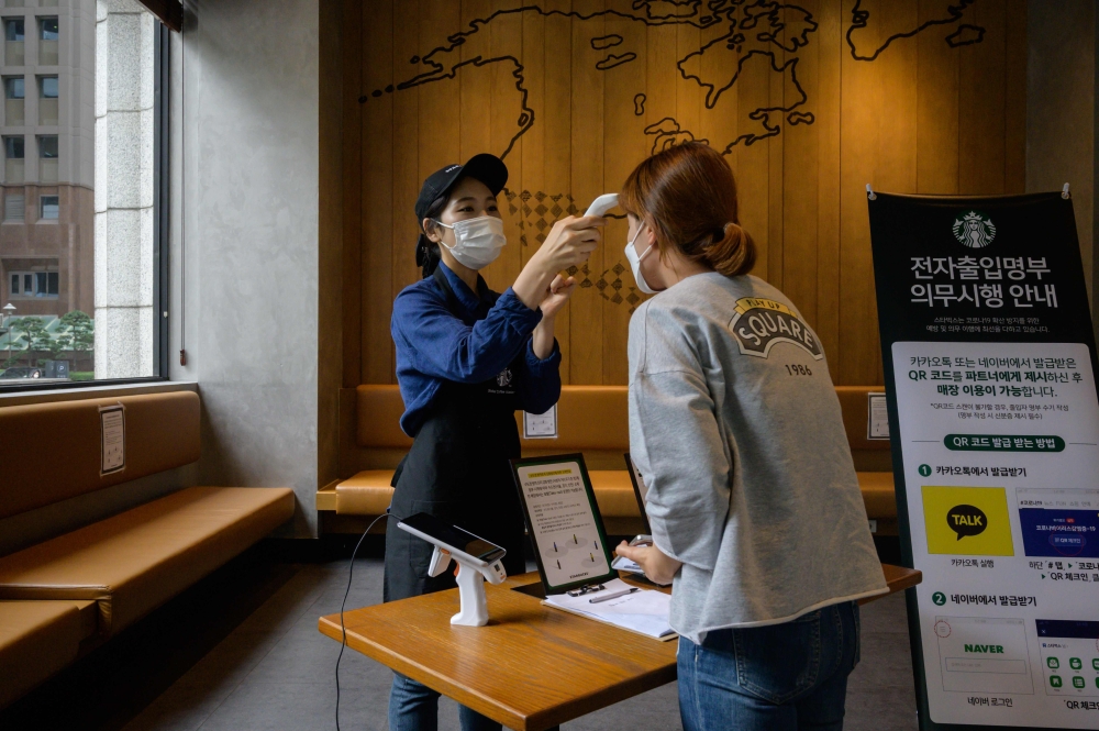 A customer has her temperature checked as a preventative measure against the COVID-19 coronavirus inside a cafe in Seoul on August 31, 2020. / AFP / Ed JONES
