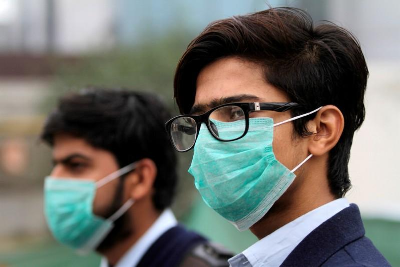 FILE PHOTO: Men wearing protective masks wait for a bus in Lahore, Pakistan November 22, 2019. REUTERS/Mohsin Raza
