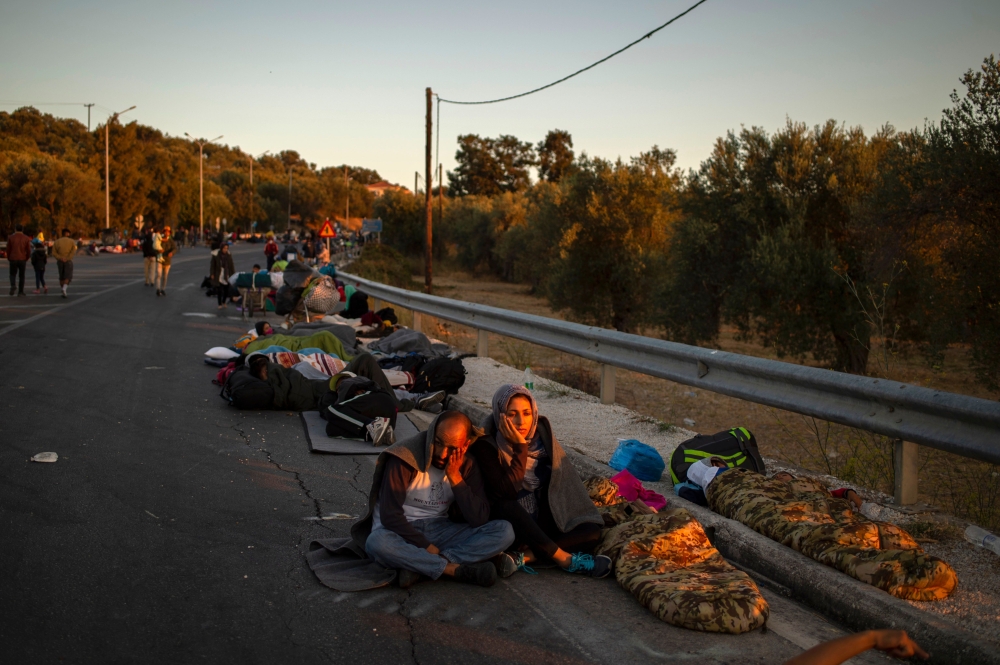 Migrants wake up as they spend the night on a road near Mytilene after a fire destroyed Greece's largest Moria refugee camp on the island of Lesbos, early on September 10, 2020.  AFP / ANGELOS TZORTZINIS
